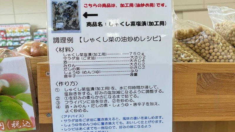 秩父の郷土食・しゃくし菜（杓子菜）の油炒めレシピを紹介する掲示物を、JAちちぶ 荒川農産物直売所『荒川そばの里』店内で撮影したもの。店内の落ち着いた雰囲気の中にレシピが掲示され、地元食材の魅力が伝わる一枚