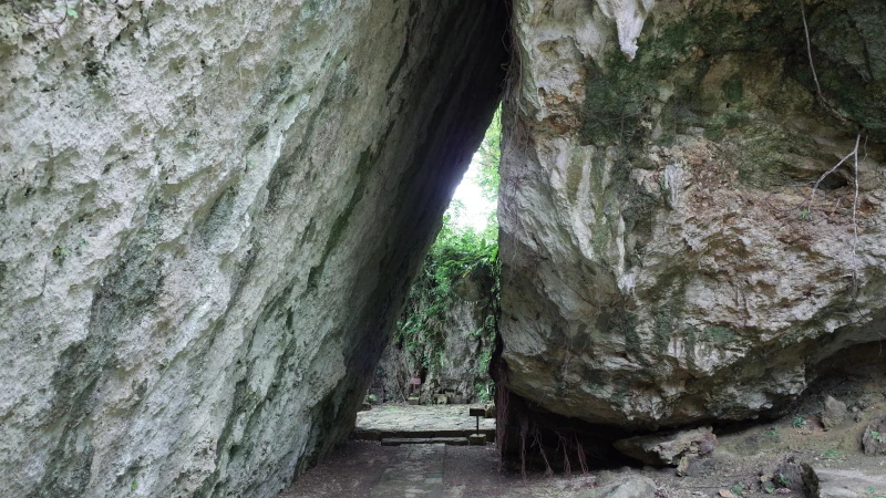 沖縄の聖地・斎場御嶽にある三庫理を撮影した画像。大きな岩が三角形に重なり合い、その奥へ続く細い通路と周囲の緑が神聖な雰囲気を感じさせる